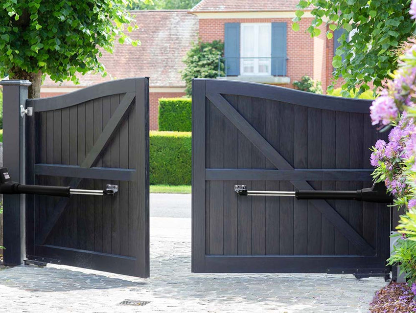 Stylish black automatic wooden gates opening to reveal a driveway leading to a red brick house with blue shutters