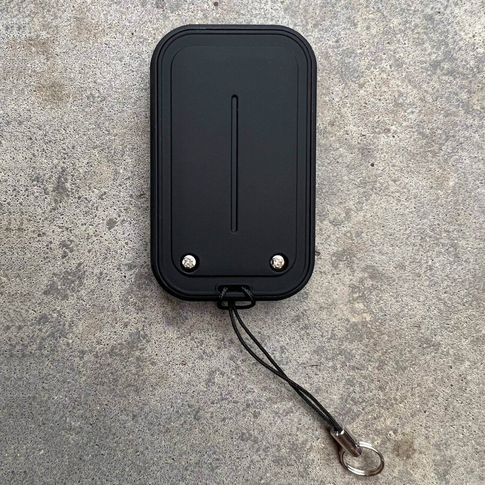 Black replacement remote with a sleek design and attachment loop on a gray surface.