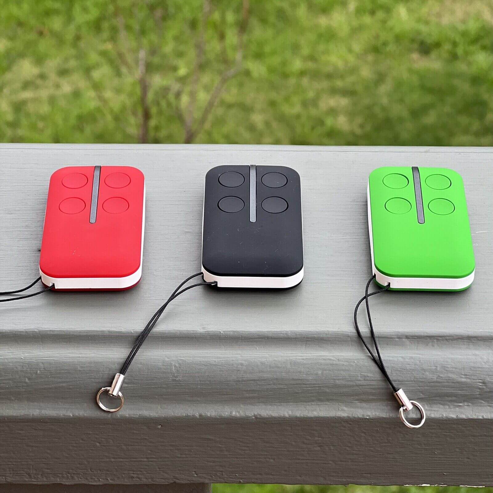 Red, black, and green HomEntry HE60 compatible garage remotes on a ledge with key rings, batteries included. Garageway remote controls.