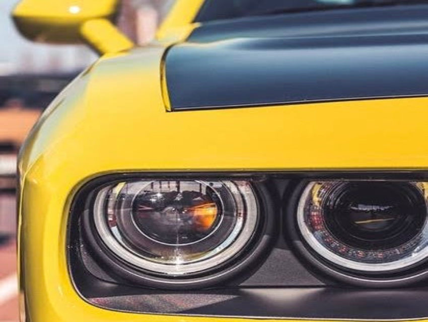 Close-up of a yellow sports car headlight with black accent, highlighting sleek design and modern engineering.