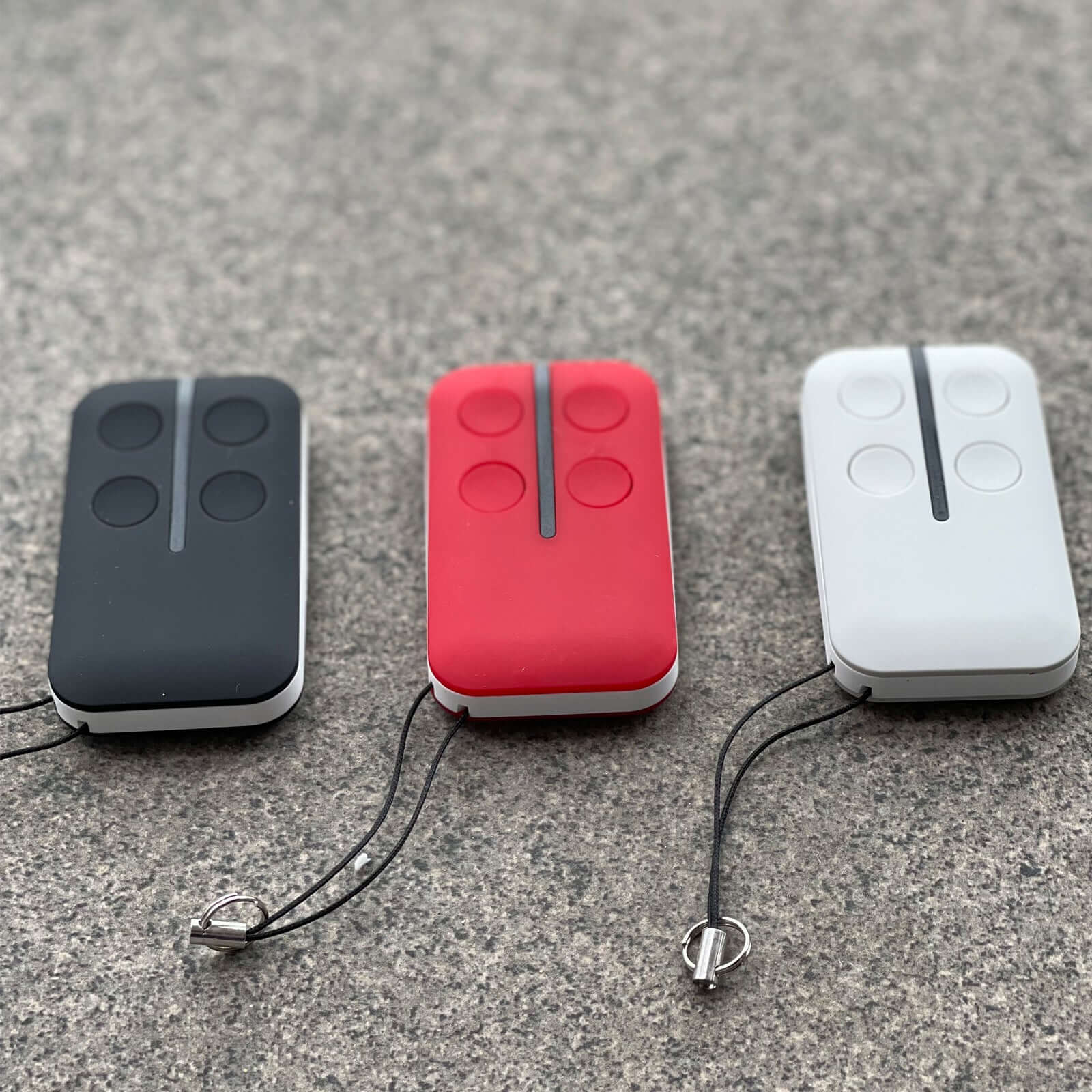 Black, red, and white BFT Mitto compatible garage remote controls with key rings on a gray surface.