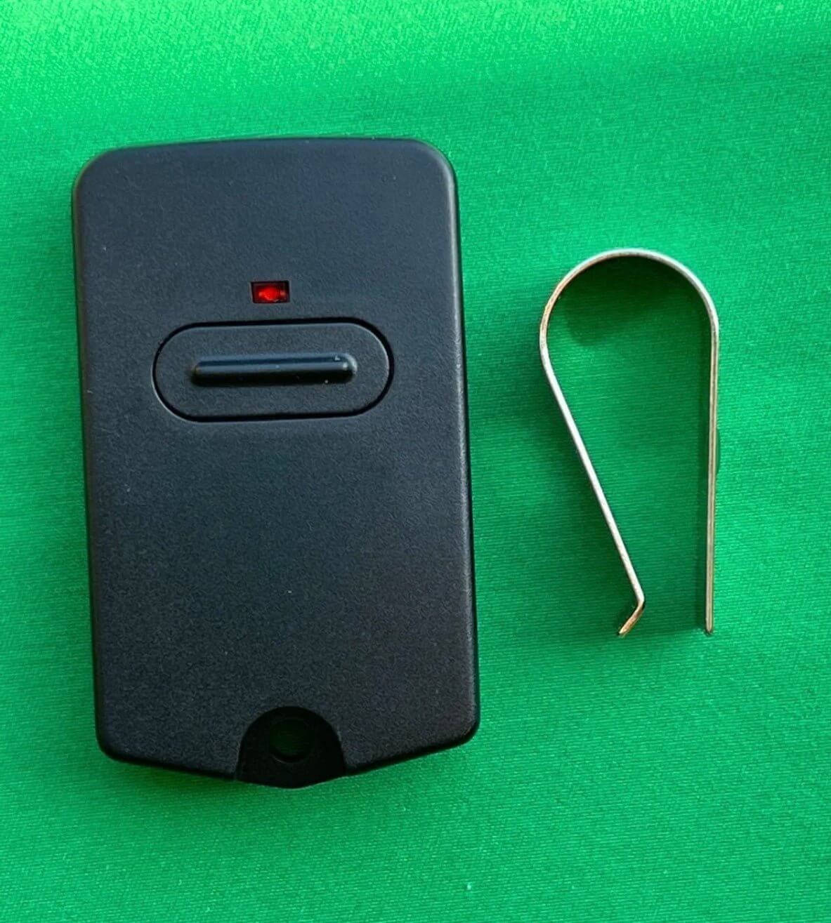 BND MPC2 TX318 compatible garage remote and clip on green background, featuring DIP switch and red button indicator. Garageway.