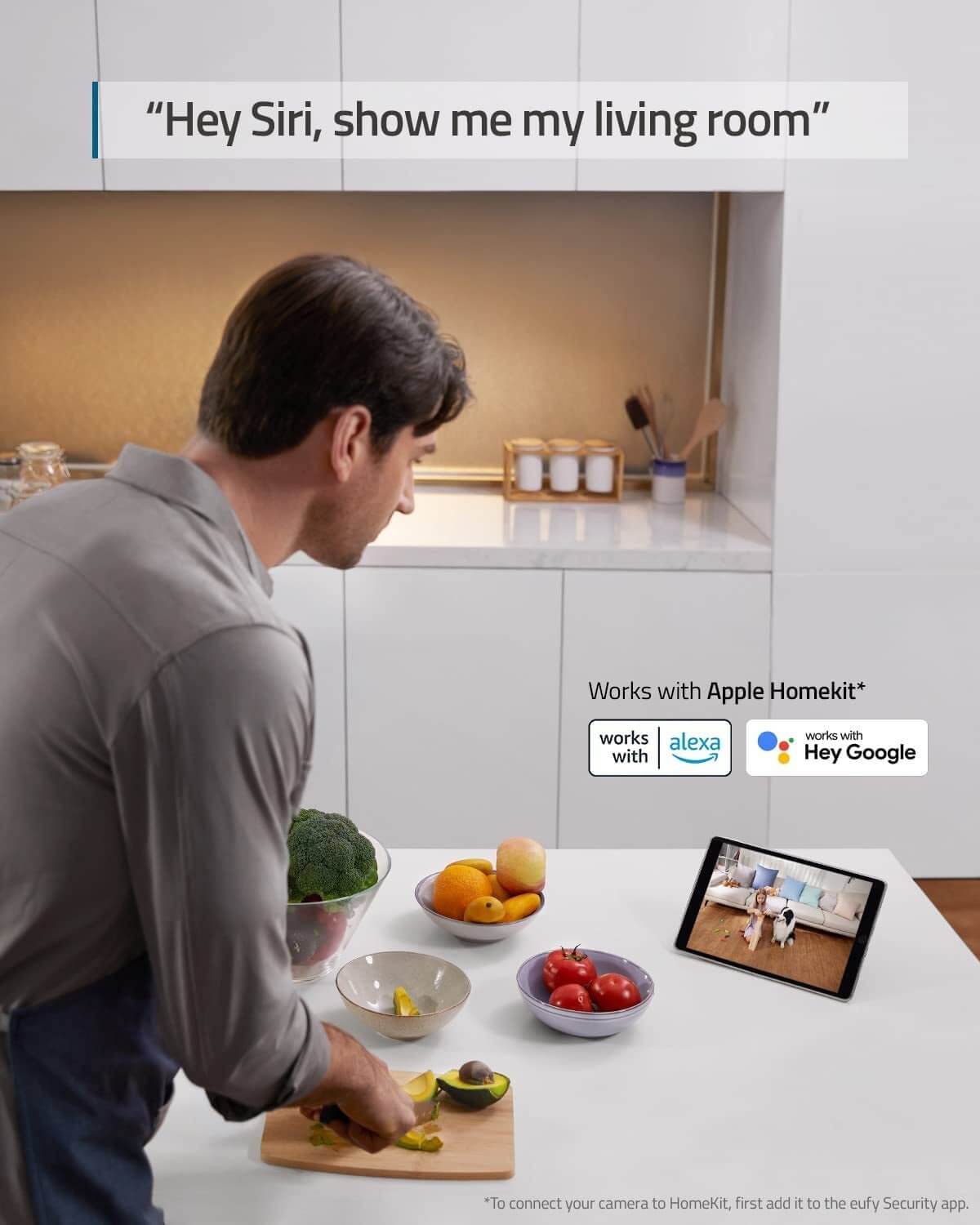 Man using voice assistant with tablet displaying indoor security camera feed in kitchen.
